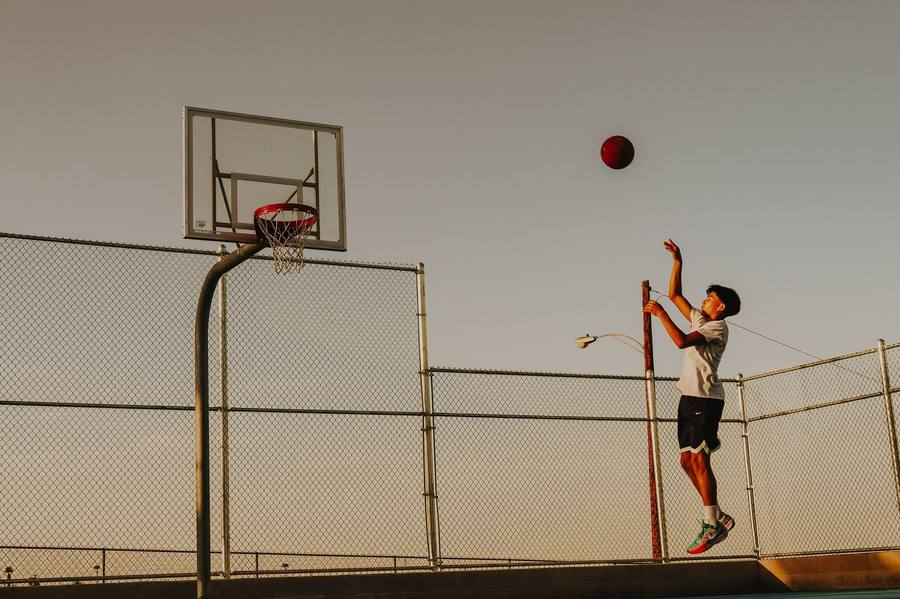 Teen athlete taking a jump shot at sunset